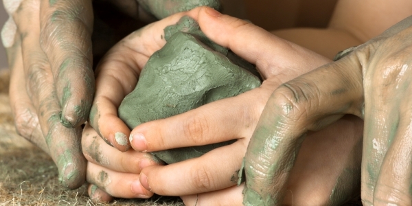 adult and child hands working with a lump of clay