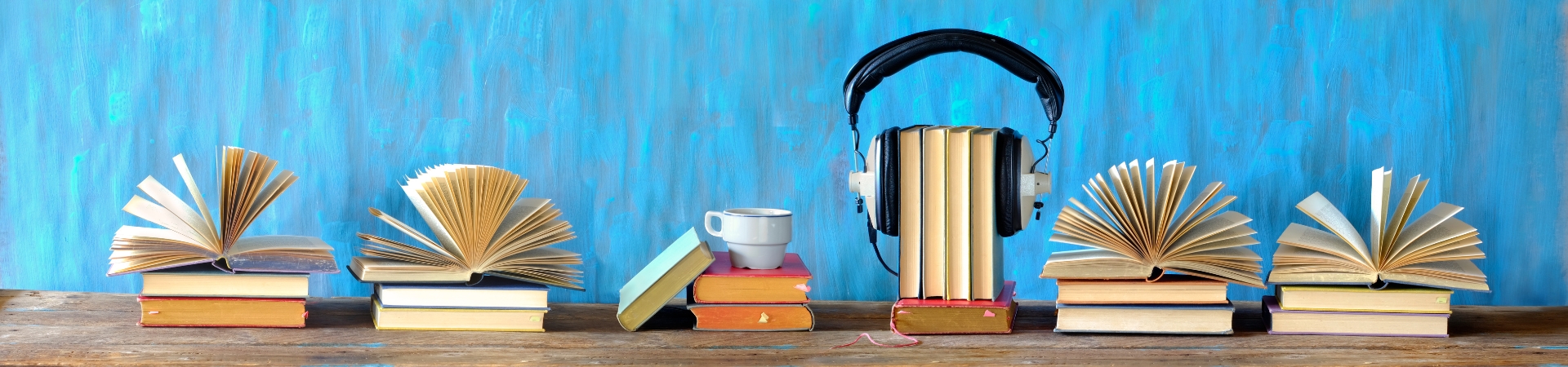 A row of books lined up in front of a blue background. One book has headphones perched on top.