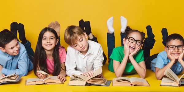 five grade-school children laying on the ground, each behind an open book.