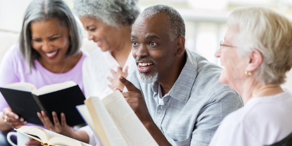 four adults holding books and sitting as a group talking