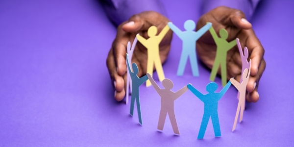 two hands embracing a circle of standing paper cutout figures in various colours