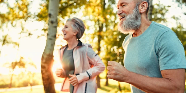 two smiling older adults jogging outside