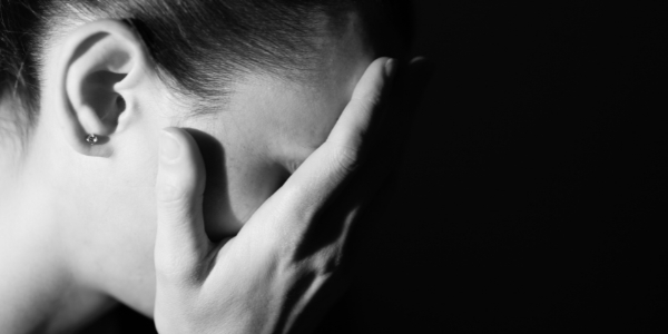adult with bowed head holding hand to face