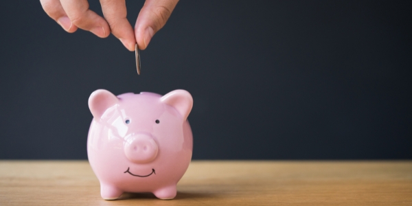 hand holding a coin above a pink piggy bank