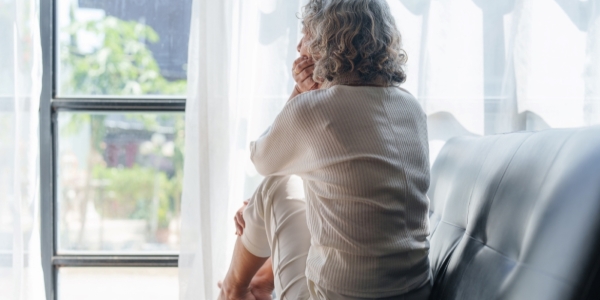 older adult sitting alone on a couch looking out a window