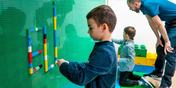two children creating at the LEGO wall with an adult watching