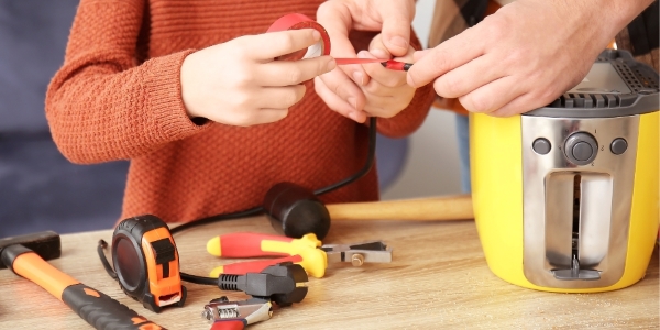 two people with assorted tools beside a yellow toaster