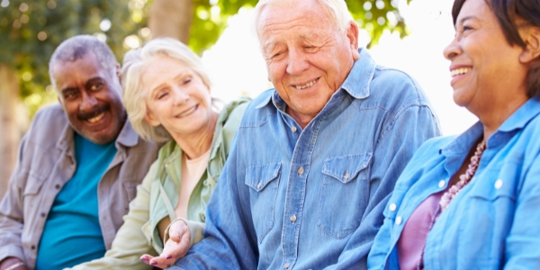 four smiling and laughing older adults sitting together outdoors