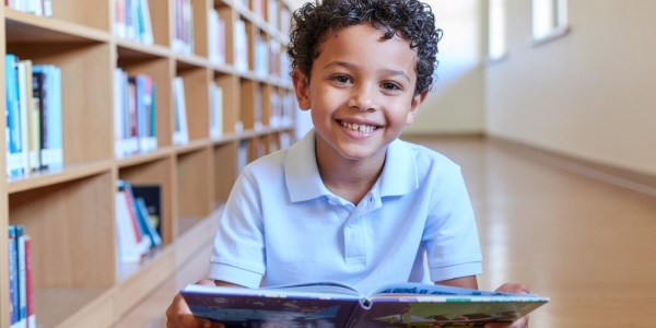 smiling young boy holding a book in a library