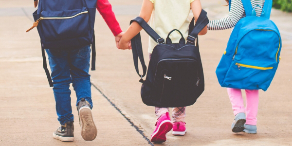 three children walking holding hands and wearing backpacks