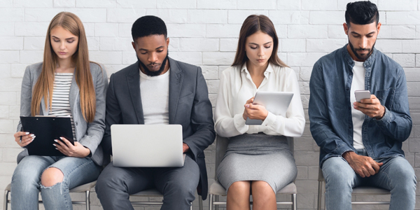 four adults seated on a bench holding various devices