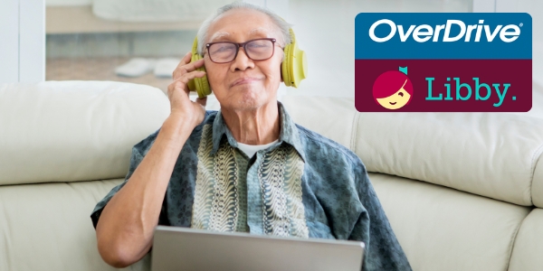 senior adult sitting on a sofa holding a laptop and wearing headphones