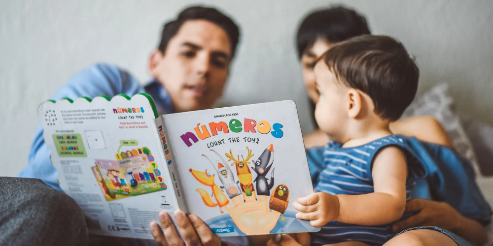 two adults and a young child sharing a picture book in Spanish