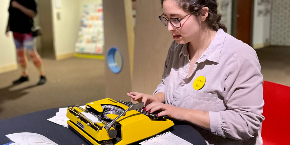 woman typing poems on yellow typewriter