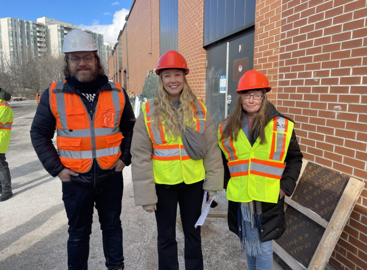 three library staff wearing hard hats and safety vests standing outside building