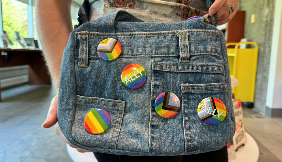 person wearing a denim bag with various Pride buttons pinned on it
