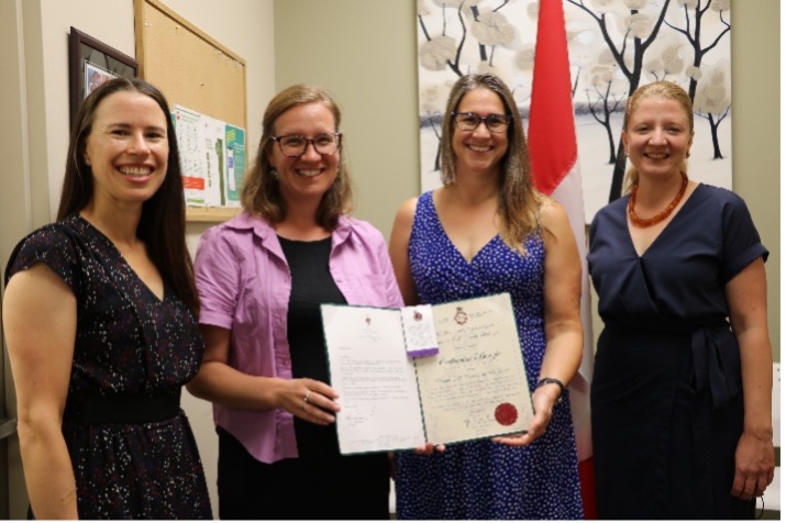 MP Karina Gould presents a folder to Catharine Benzie. Lindsay Zalot and Lita Barrie stand on either side.