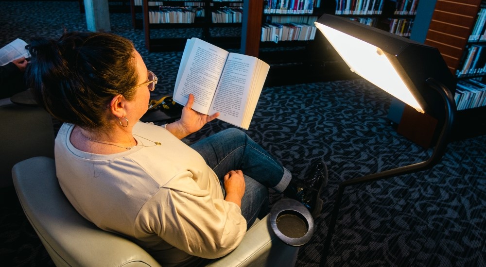 adult reading a book facing a light therapy lamp