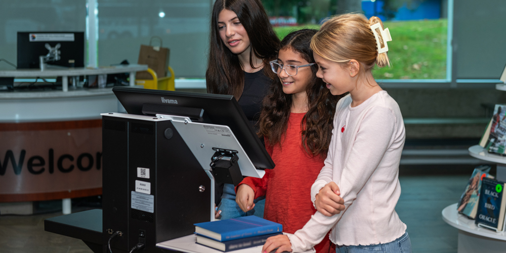 three young adult borrowing books at self-checkout