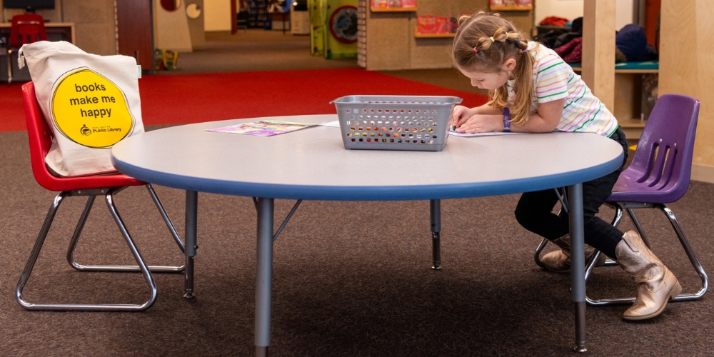 child colouring at a table with canvas tote on a chair