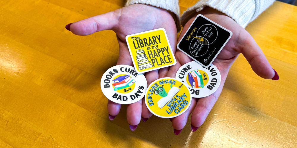 two hands holding five assorted library stickers