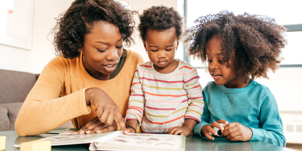 A mom and two children gather around a picture book, pointing at images