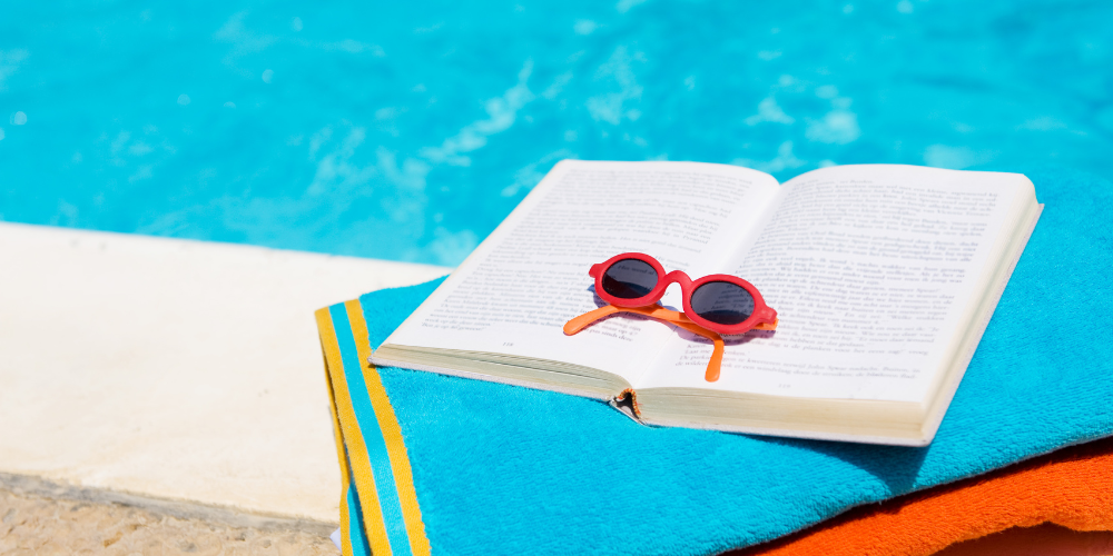 Library book open on a towel beside a pool