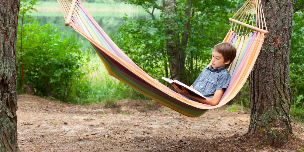 A child in a hammock reading a book.