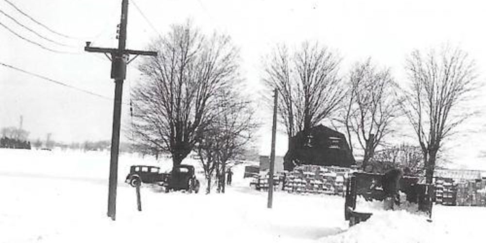 black and white photograph of a farm with three buildings covered in snow