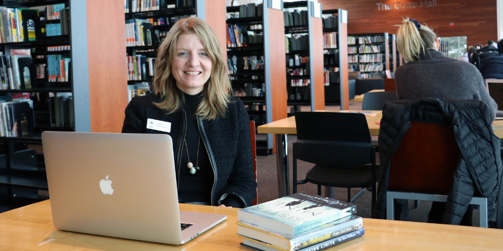 CEO Lita Barrie sits at a laptop in front of shelves of books