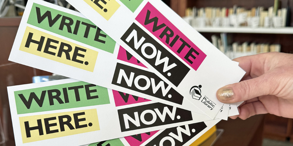 handing holding a number of Write Here Write Now bookmarks