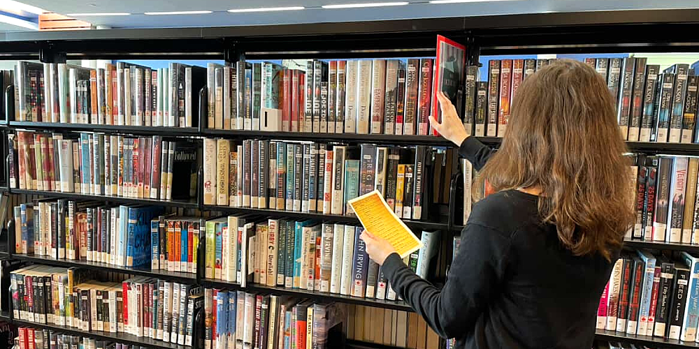 A person holds a piece of paper containing a puzzle mystery while surrounded by books.