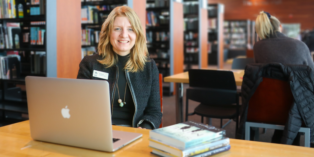 BPL CEO, Lita Barrie, smiles at the camera from behind a laptop.