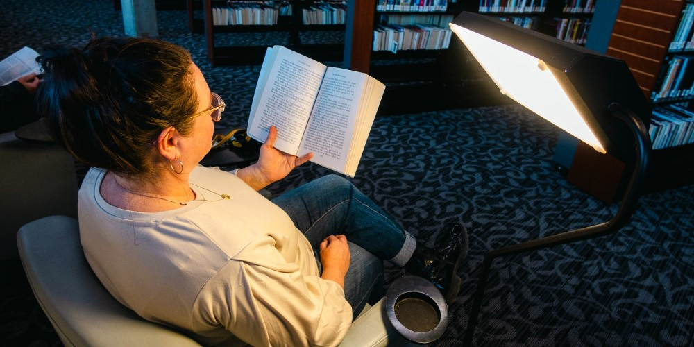 adult reading a book and using a light therapy lamp