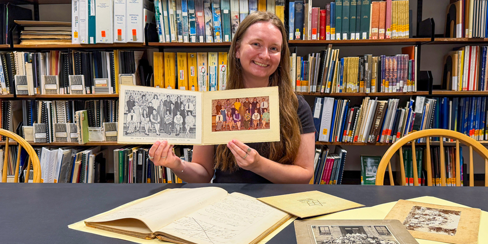 seated staff holding a vintage photo with other historical artifacts on a table