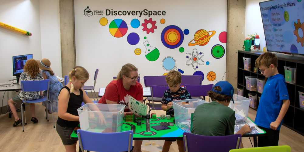 adult and six children working on activities at DiscoverySpace tables.