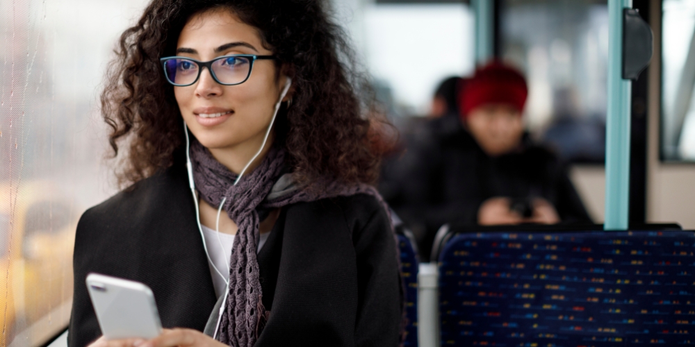 adult wearing earphones and holding a device, looking out a train window