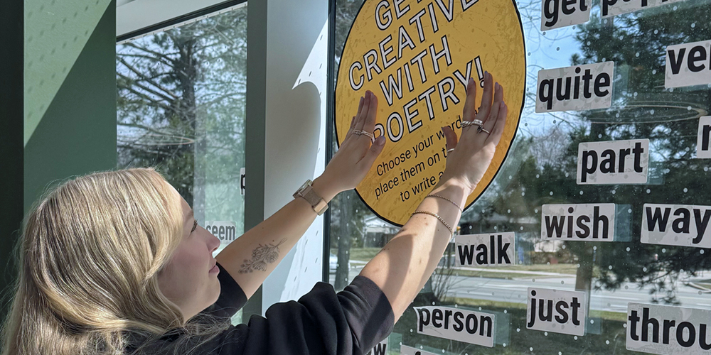 BPL staff member reaching up to put a decal on a window, Get Creative with Poetry.