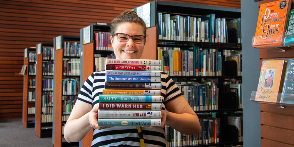 smiling staff member holds a stack of 10 books