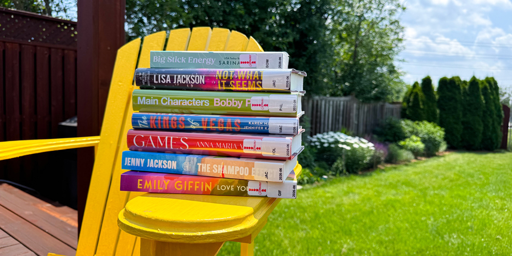 stack of books on the arm of a yellow deck chair in a grassy backyard