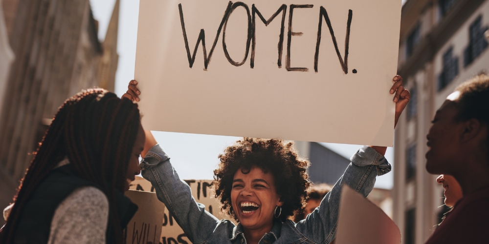 woman holding up a sign with displayed text saying Women.