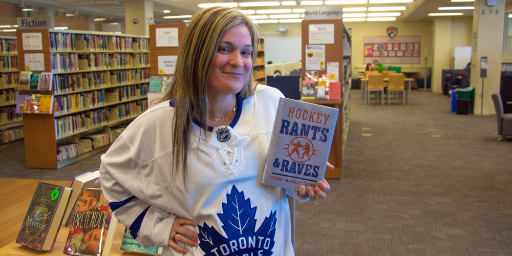 Alton Branch Librarian Heather standing in library holding Hockey Rants & Raves.