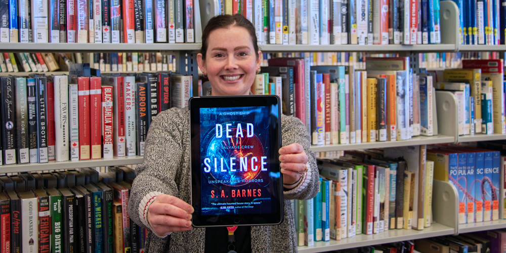 Librarian Sarah standing in front of bookshelf holding book