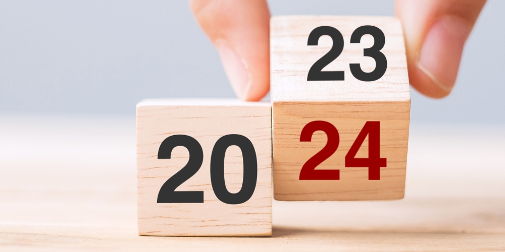 a wood block painted with the number 20 beside another block displaying a 23 on one side and 24 on another side. Two fingers are turning the block from the 23 side to the 24.