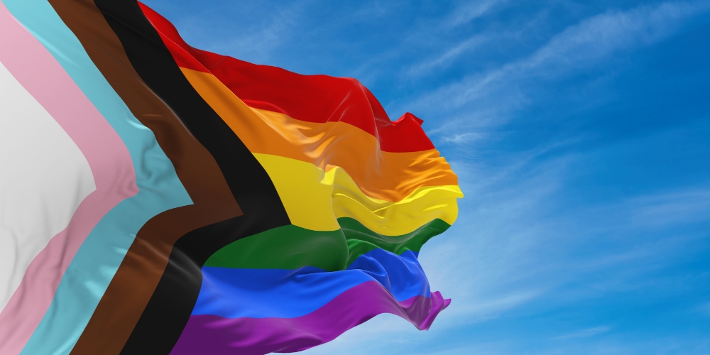 progress pride flag against a blue sky background