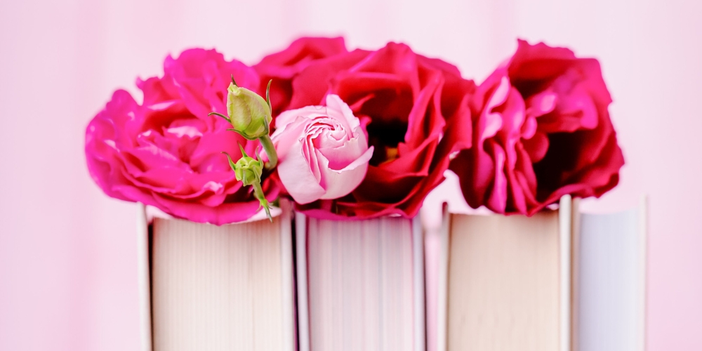 three hadcover books with pink roses resting on the top edge