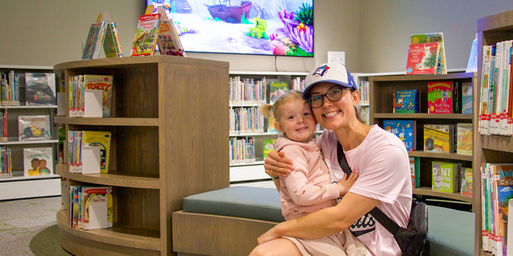 seated adult holding toddler near shelves of picture books