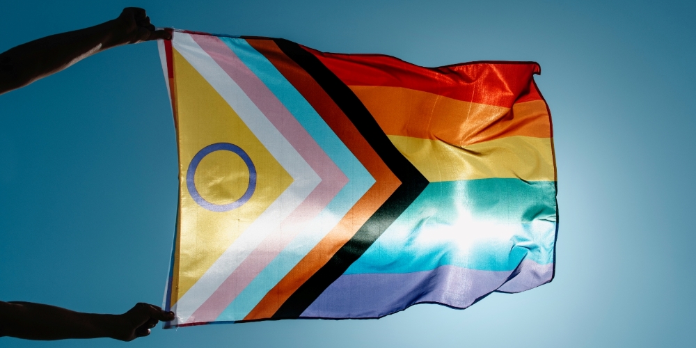 two extended arms holding an intersex progress pride flag against a blue sky background