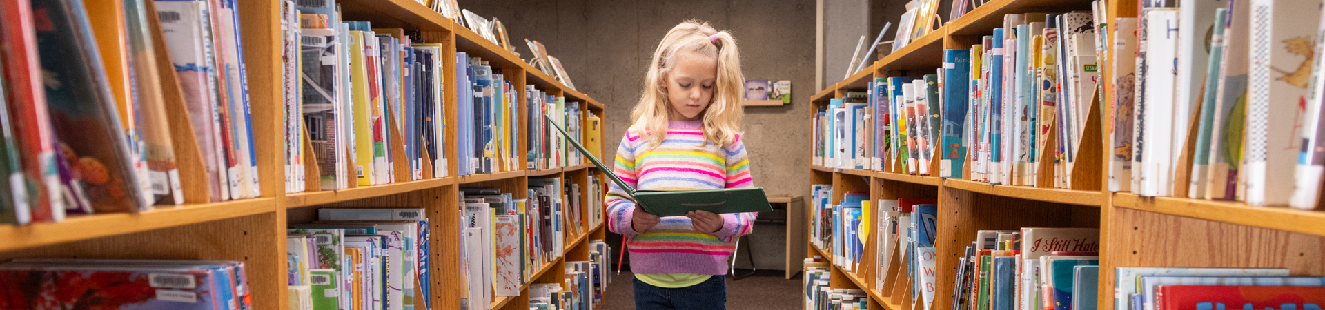 child standing in book stack reading a book