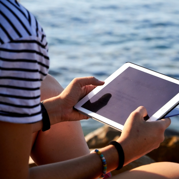 adult sitting near water and holding a tablet